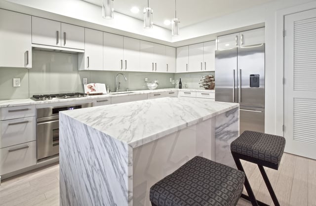 Modern kitchen with marble island and stainless steel appliances.