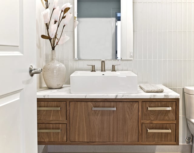 Modern bathroom vanity with wood cabinets, white countertop, vessel sink, and decorative vase.