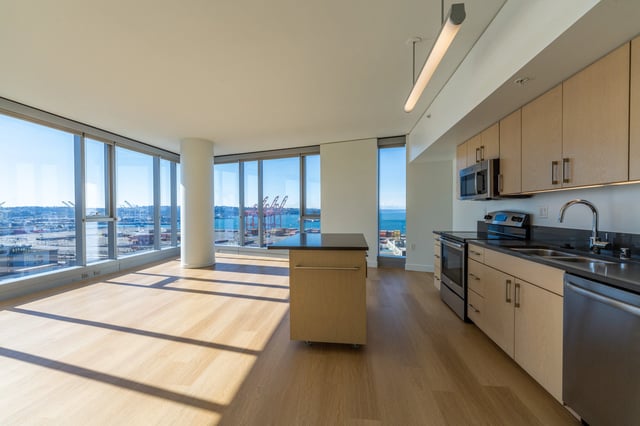 Modern kitchen and living area with floor-to-ceiling windows overlooking a harbor with cranes.