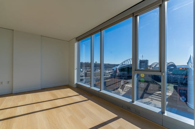 Empty room with hardwood floors and a large window overlooking a city stadium.