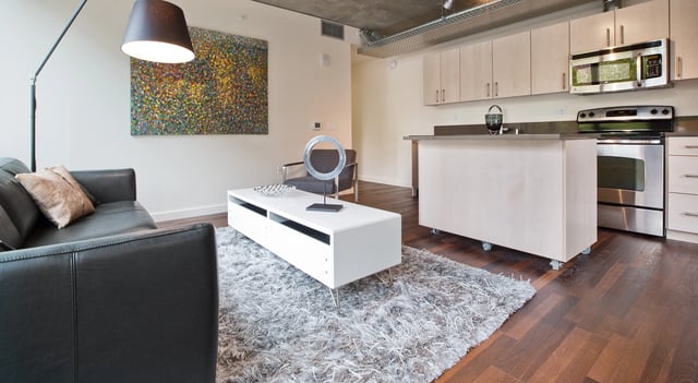 Modern living room and kitchen area with dark leather couch, white coffee table, and stainless steel appliances.