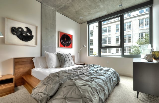 Modern bedroom with king-size bed, art, and large window with city view.
