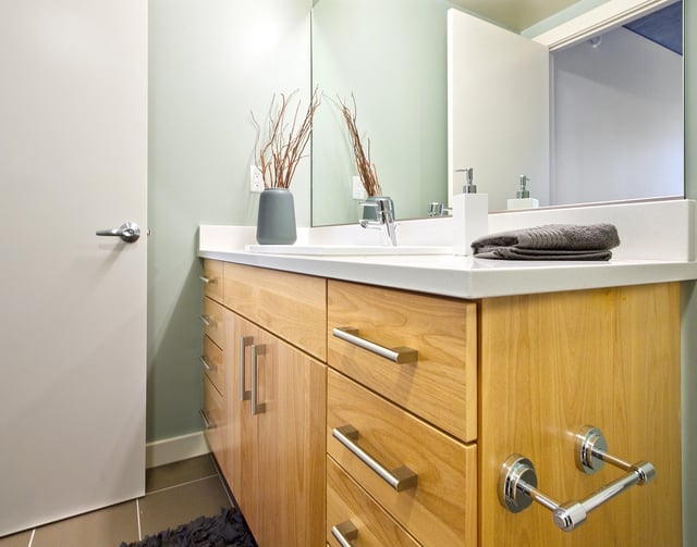 Modern bathroom vanity with wood cabinets, white countertop, sink, and mirror.
