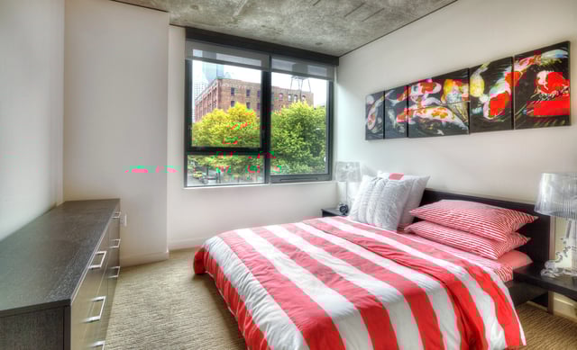 Bedroom with a king-size bed, dresser, and a window with a city view.