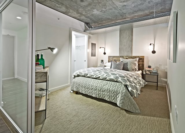 Modern bedroom with a queen-size bed, minimalist nightstand, and concrete ceiling.