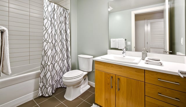 Modern bathroom with white vanity, wooden cabinets, and a patterned shower curtain.