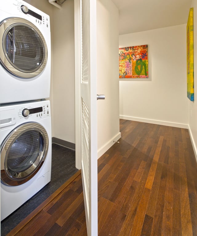 Stacked washer and dryer in laundry closet with hardwood floors.