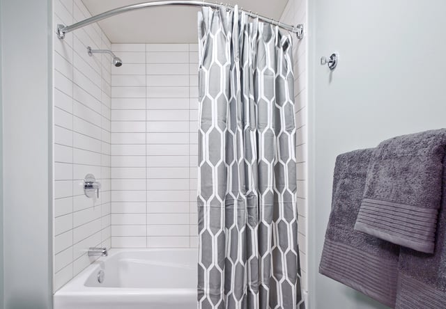 Modern bathroom with a white bathtub and grey patterned shower curtain.