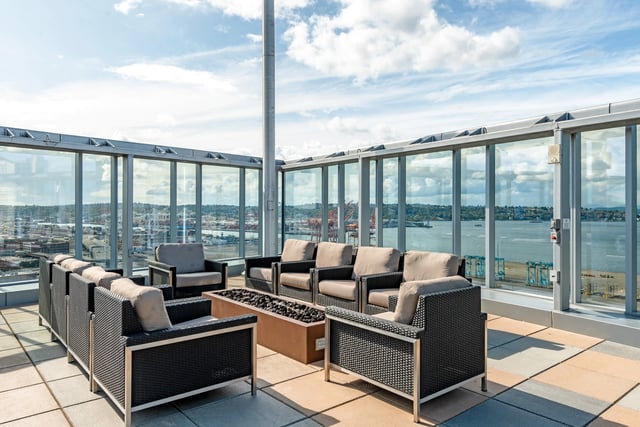 Rooftop lounge area with seating and a fire pit overlooking a bay and city skyline.