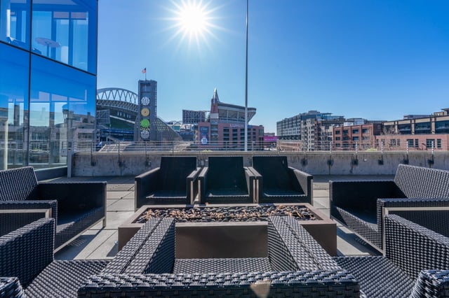 Rooftop patio with seating and a fire pit overlooking a stadium.