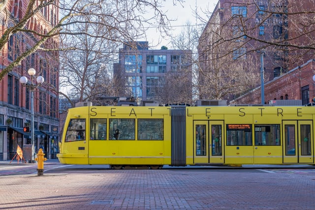 Yellow Seattle streetcar on a brick street with trees and buildings.