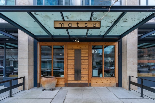 Exterior entrance of the Matsu building, featuring wooden doors and a modern glass awning.