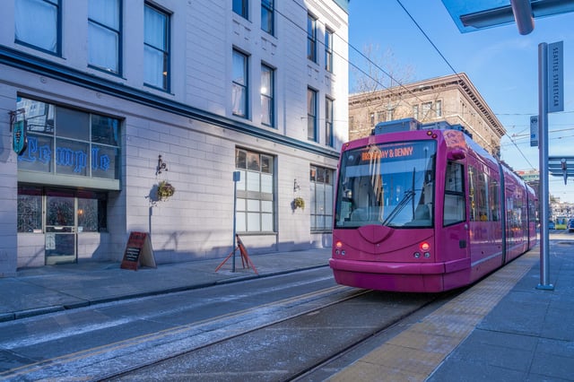 A pink streetcar passes a building with the word "Temple" in the window.
