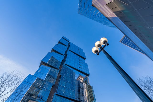 Modern glass apartment building exterior with a streetlamp in the foreground against a clear blue sky.