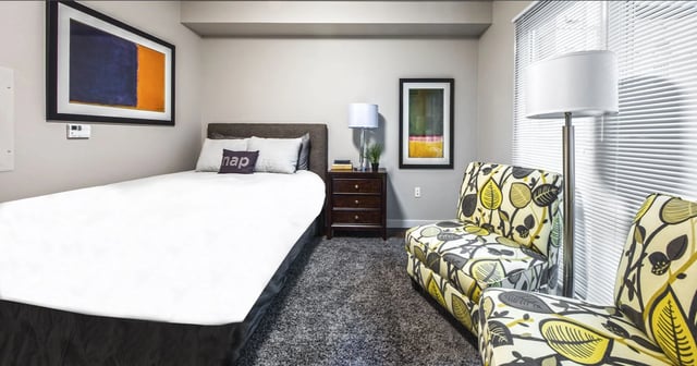 Bedroom with a queen bed, two accent chairs, and artwork.