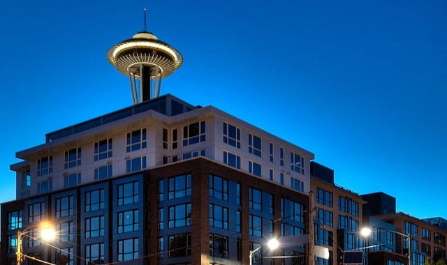 Modern apartment building with the Space Needle in the background at dusk.