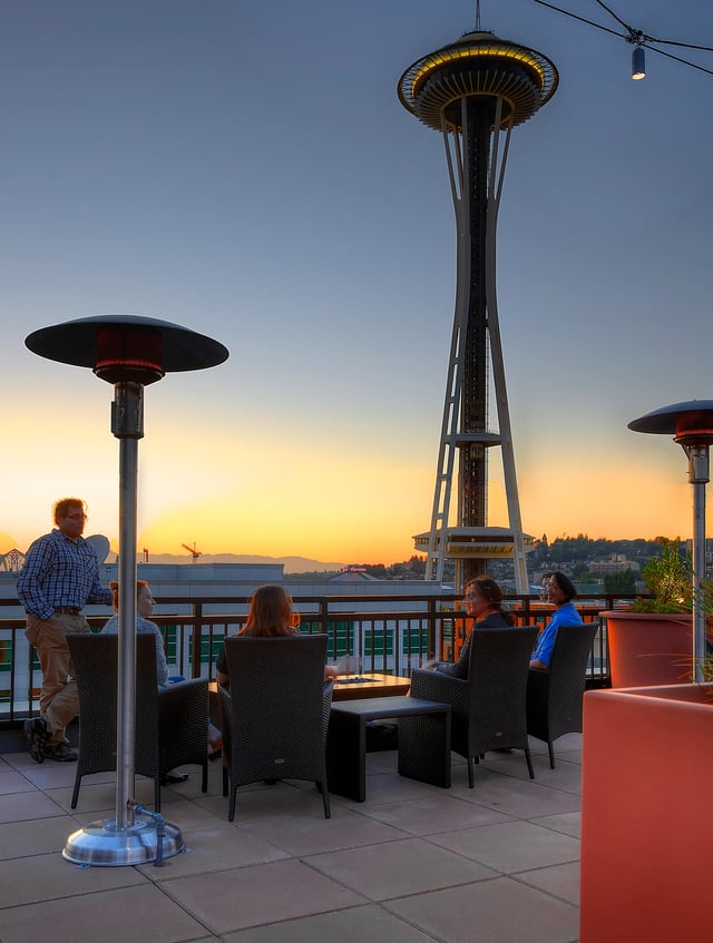 Rooftop deck with Space Needle view and people relaxing at sunset.