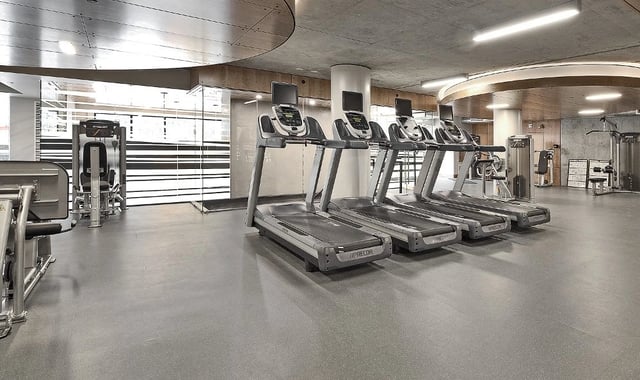 Row of treadmills in a modern apartment gym with weight machines visible in background.
