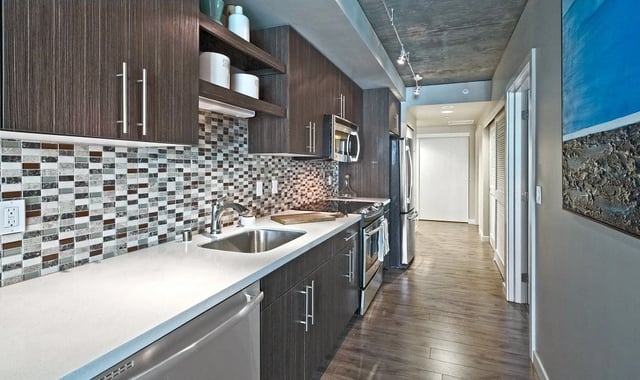 Modern galley kitchen with dark wood cabinetry, quartz countertops, and a mosaic tile backsplash.