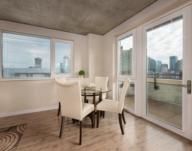 Dining area with a glass-top table and four upholstered chairs, overlooking a cityscape.