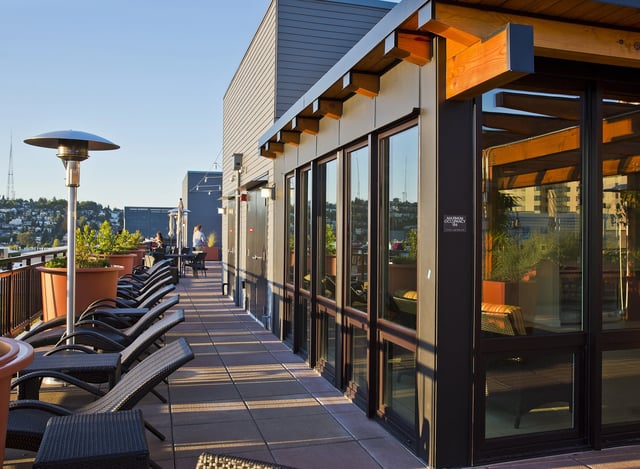 Rooftop terrace with lounge chairs and tables, overlooking a city skyline at sunset.