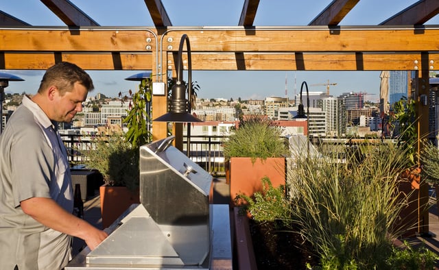 Man grilling on a rooftop patio with a city skyline view.