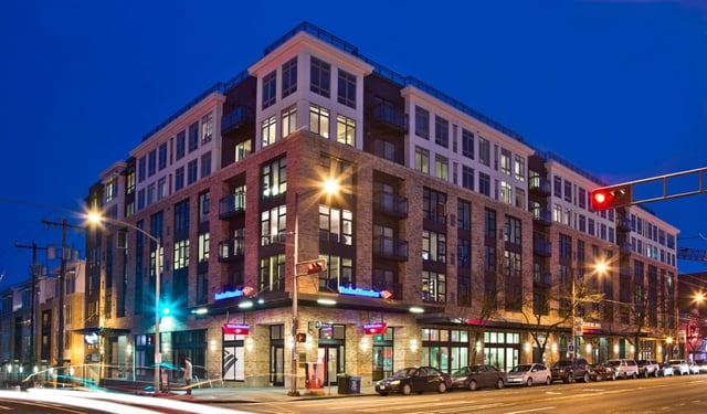 Modern apartment building exterior at dusk with streetlights and cars.
