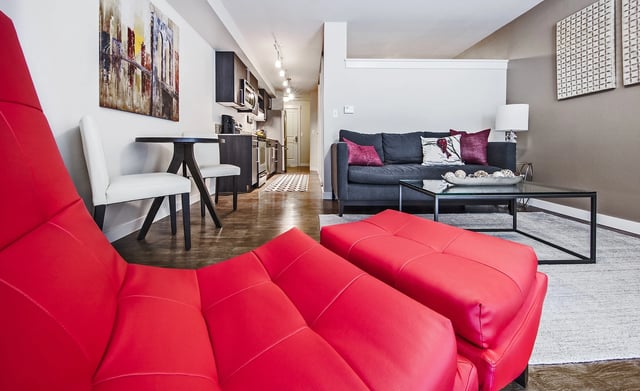Modern living room and kitchen area with red and gray furniture, and artwork on the wall.