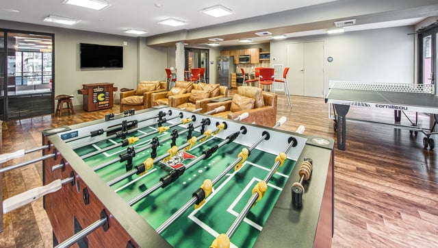 Foosball and ping pong table in a common room with leather seating and a television.
