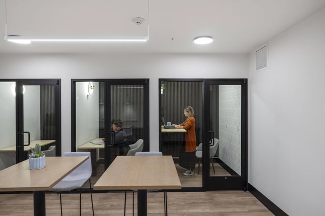 A modern co-working space with glass-walled private offices and a communal work area.