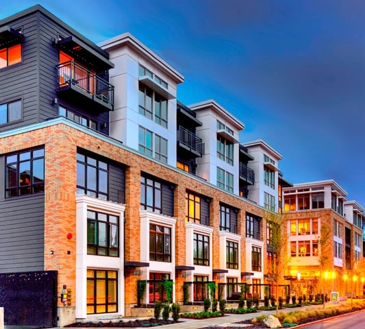 Exterior of a modern apartment building with brick and dark siding, balconies, and large windows at dusk.