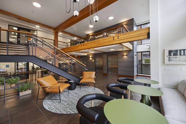 Modern lobby with exposed wood beams, a floating staircase, elevators, and seating areas.