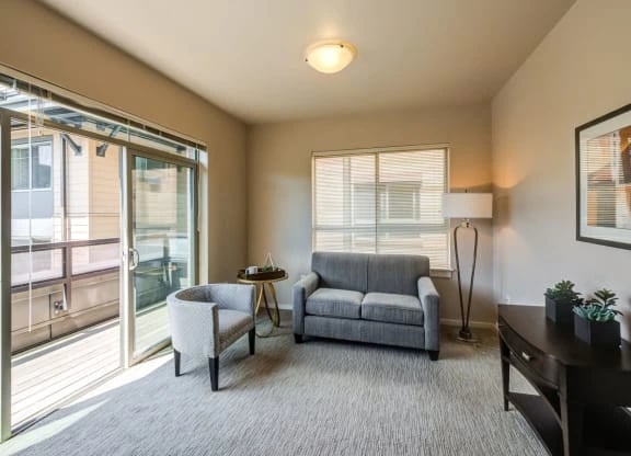 Apartment living room with a sofa, two chairs, a sliding glass door to a balcony, and a floor lamp.