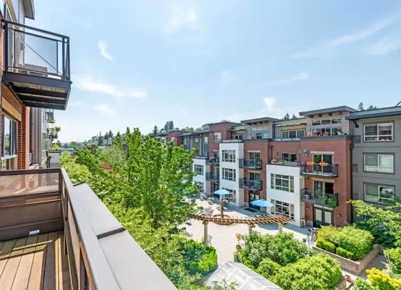 Balcony view of a modern apartment community courtyard with trees, walkways, and lounge seating.