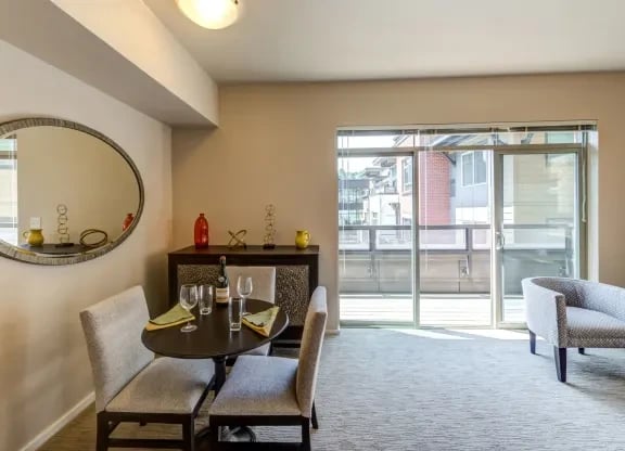 Interior dining area of an apartment with a round table, chairs, and a sliding glass door to a balcony.