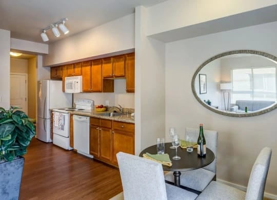 Open-concept kitchen and dining area in an apartment with wooden cabinets, stainless appliances, and a round wall mirror.