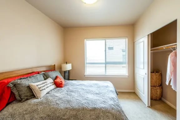 Bedroom in an apartment with a bed, pillows, nightstand, window, and open closet.