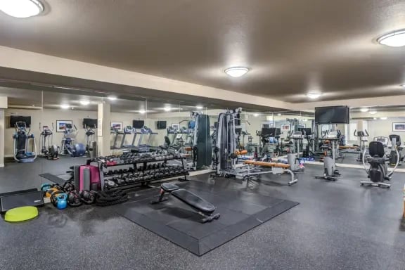 Indoor apartment community gym with treadmills, weights, and a workout mat.