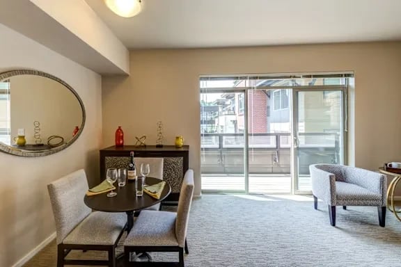 Interior dining area with round table, four chairs, wall mirror, and sliding glass door to balcony.