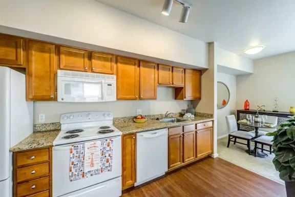 Kitchen with wooden cabinets, granite countertops, and white appliances in an apartment.