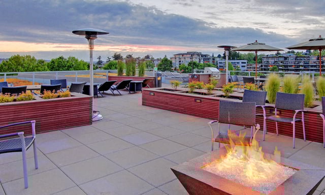 Rooftop patio with fire pit, lounge chairs, and grills at dusk.