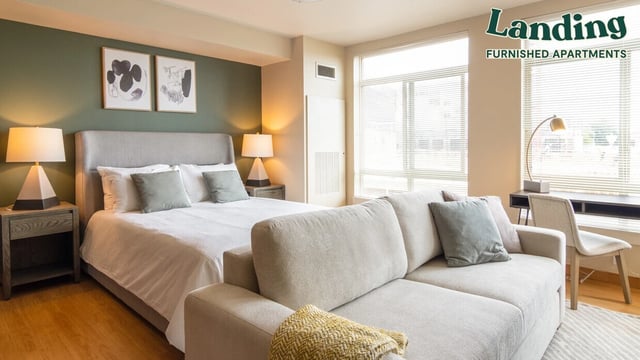 A furnished studio apartment with a bed, sofa, and desk.