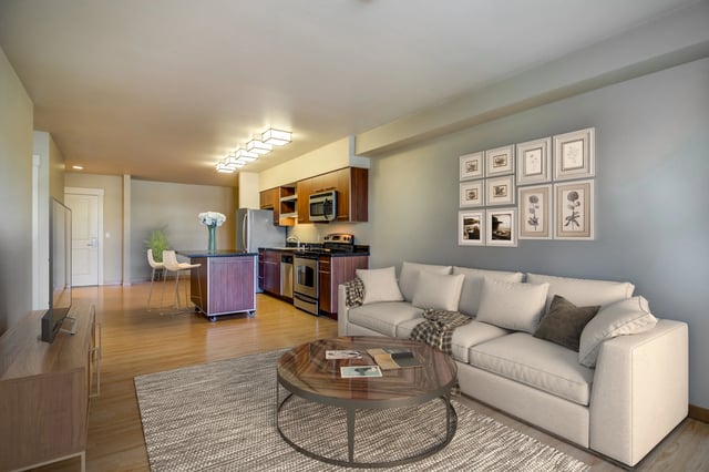 Living room and kitchen of an apartment with white couch, island, and stainless steel appliances.