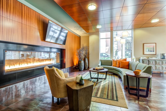 Modern apartment lobby with a sleek fireplace, comfortable seating area, and large windows.