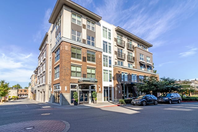 Modern apartment building exterior with brick and siding, balconies, and parking.