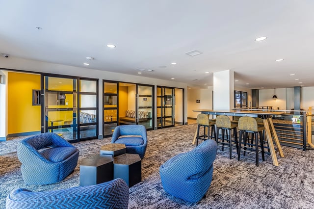 Modern lounge area with blue armchairs, hexagonal coffee tables, and a high-top bar with stools.