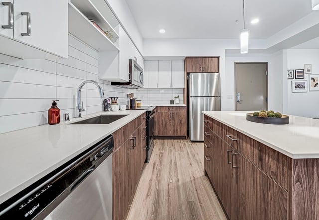 Modern kitchen with stainless steel appliances, white countertops, and wood cabinetry.