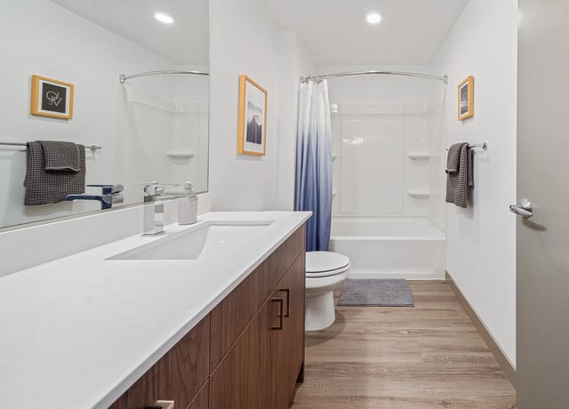 Modern bathroom with double vanity, large mirror, toilet, and bathtub with shower curtain.