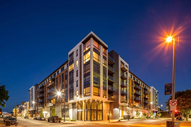 Modern apartment building exterior at dusk with illuminated windows.