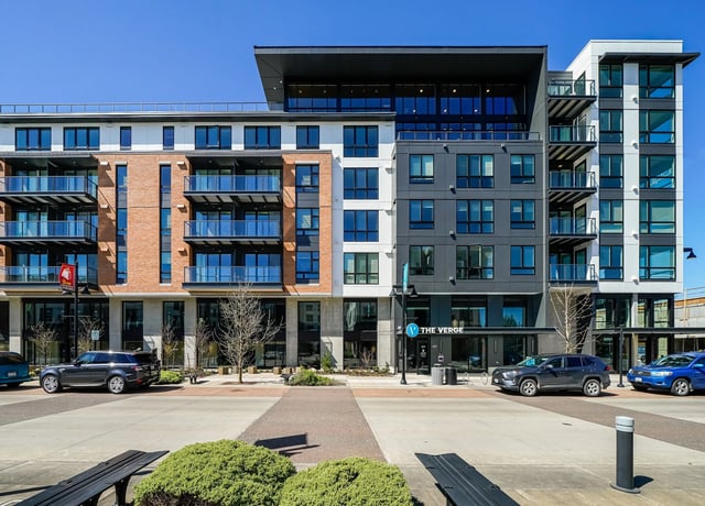 Exterior view of The Verge apartments, featuring modern architecture with brick and dark grey siding, balconies, and street-level retail.